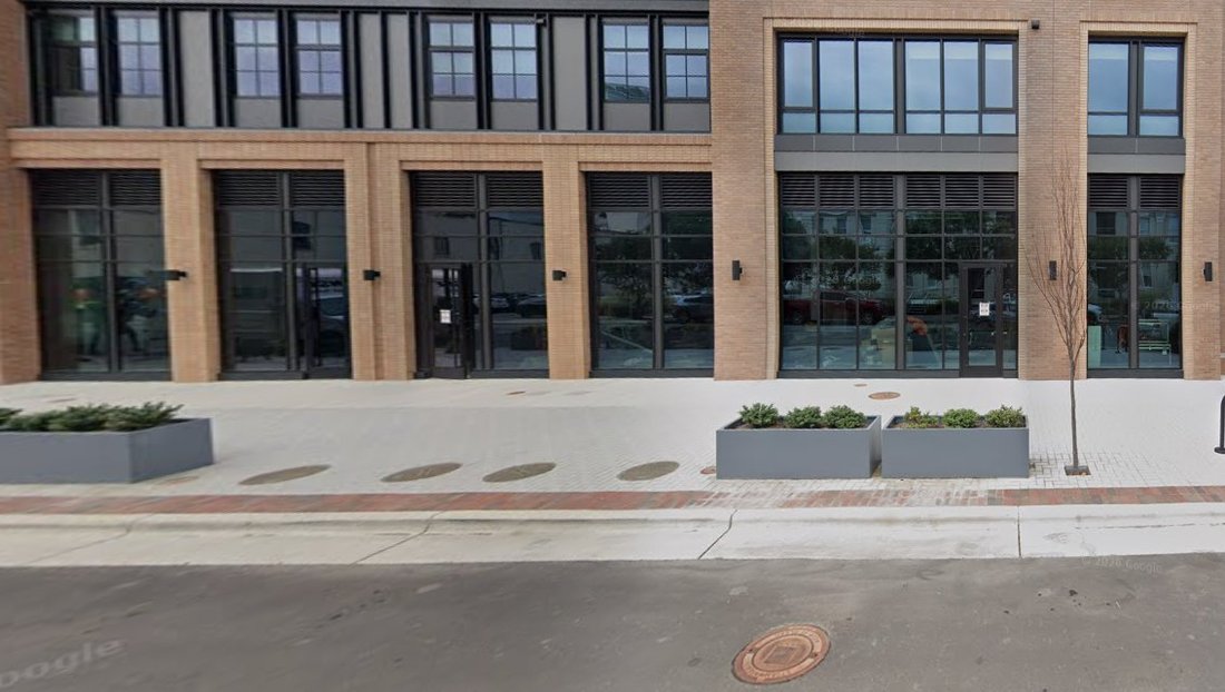 Street view of the NOVUS building exterior, brick facade with large black-framed windows and planter boxes